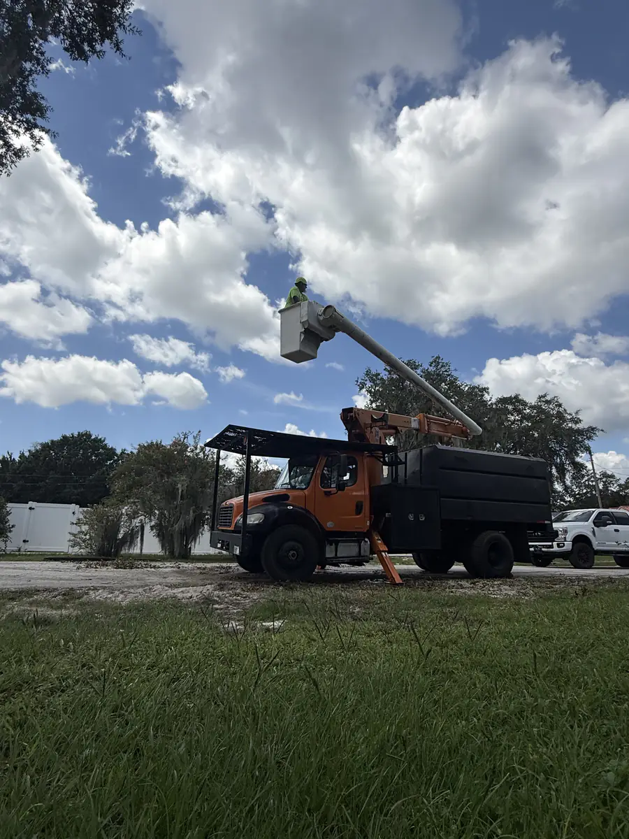 Orange forestry bucket truck with a chip box parked on its outriggers beside the cleared Deltona lot as the boom comes down