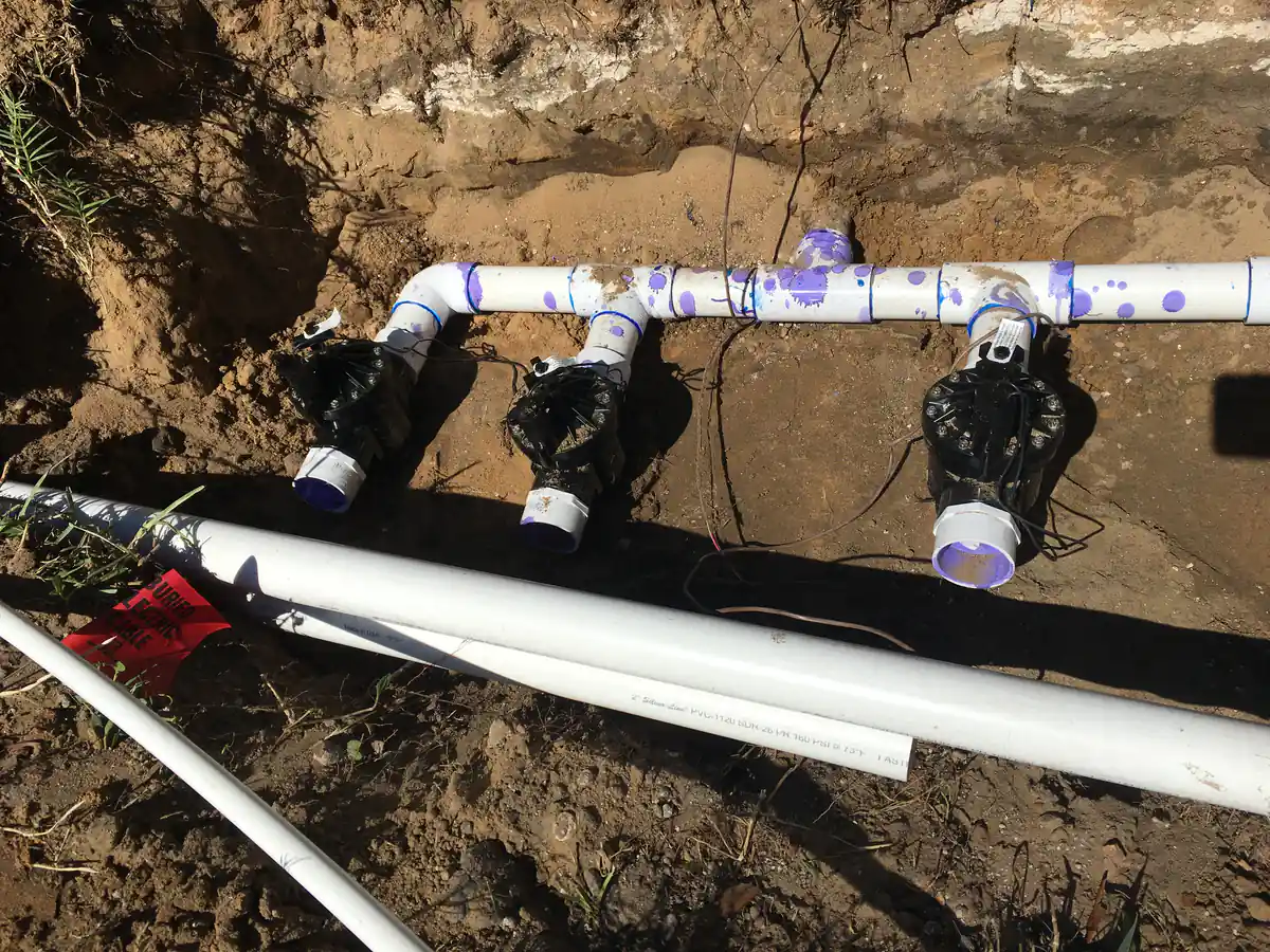 Three inline irrigation valves assembled on schedule 40 PVC in an open trench with control wire alongside