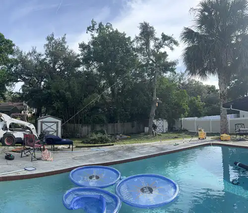 Wide shot from behind the pool showing the rigging line and the skid steer staged across the DeLand yard